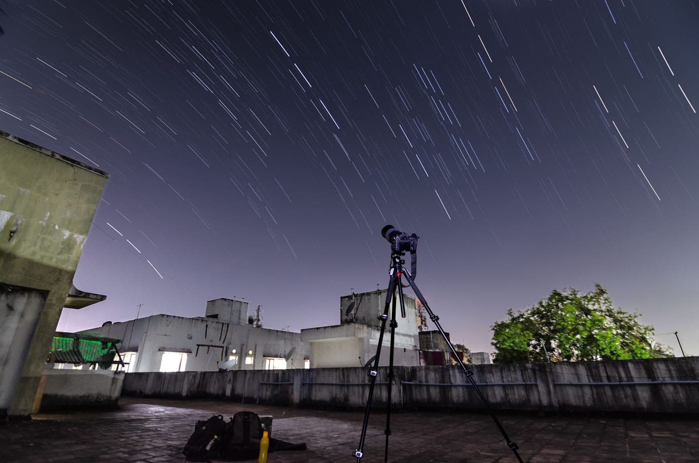A telescope on a rooftop beneath star trails in a long night exposure