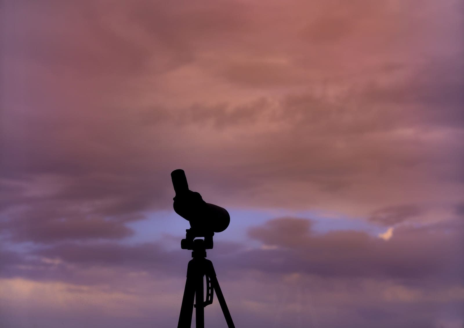 A telescope on a tripod silhouetted against a cloudy sunset sky