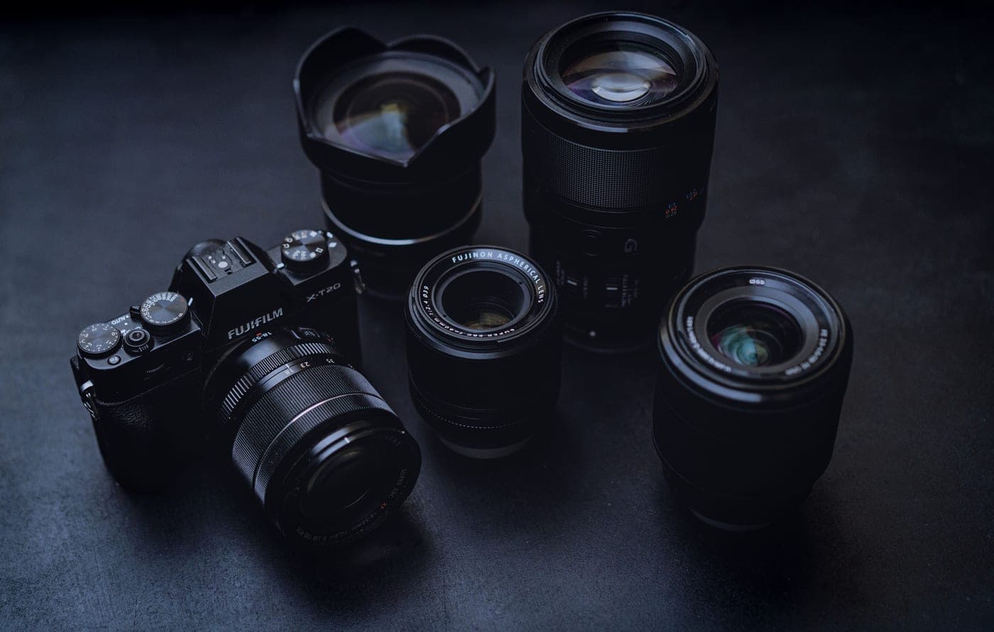 A camera body and several lenses of different focal lengths on a dark table