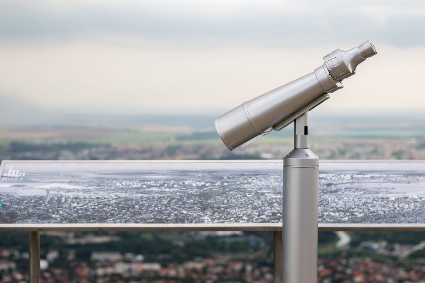 A mounted viewing telescope with a blurred landscape behind it