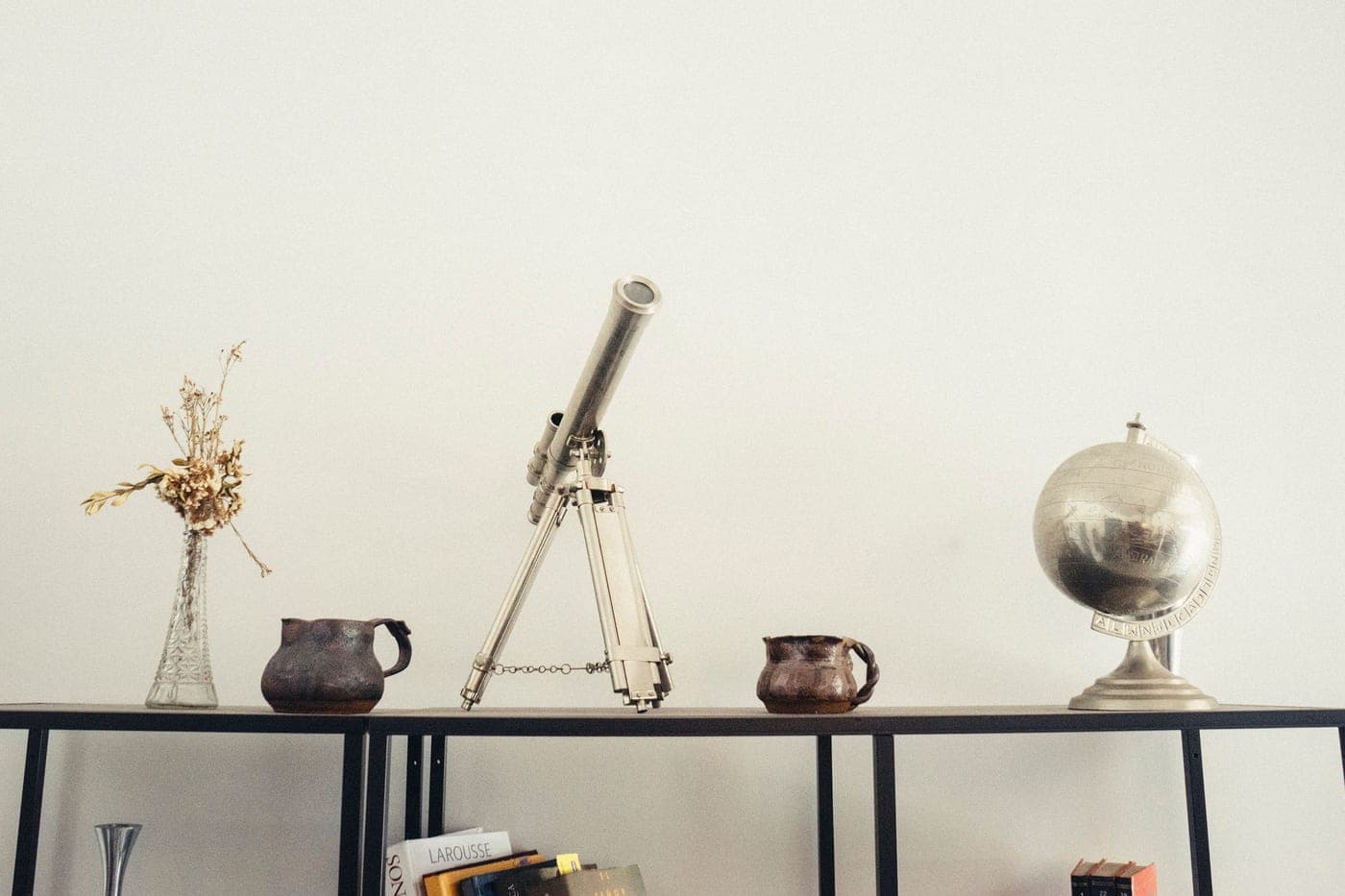 A telescope, a globe and books arranged on a shelf as decoration